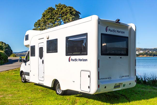 White Pacific Horizon campervan parked on a grassy field beside a lake under a clear blue sky.