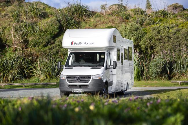 White Pacific Horizon Mercedes-Benz campervan parked on gravel against a backdrop of green hills.