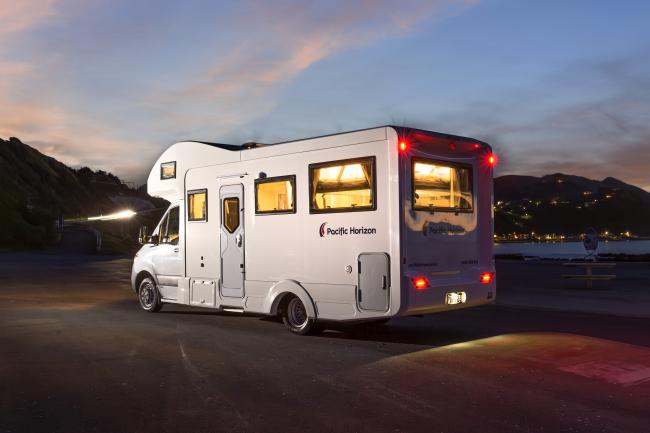 White Pacific Horizon campervan parked at dusk with glowing interior lights and tail lights.