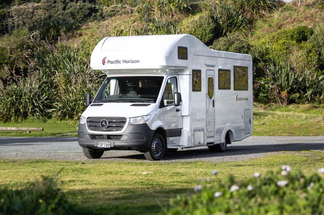 White Pacific Horizon Mercedes-Benz campervan parked on gravel with green hills in the background.