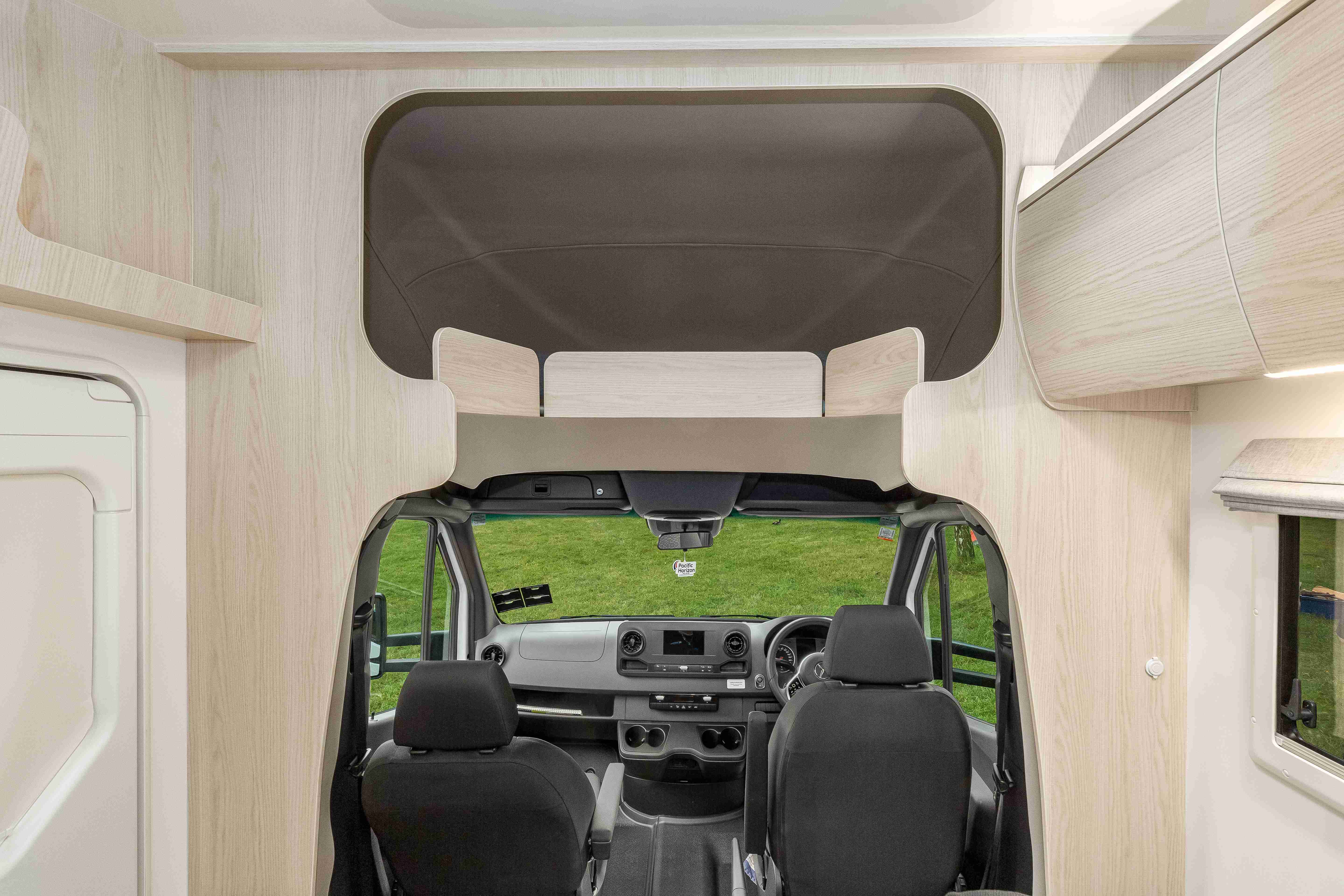 Campervan interior looking forward past two grey cab seats to a light timber-look over-cab sleeping area.