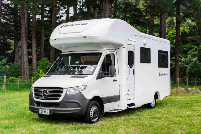 White Pacific Horizon Mercedes-Benz campervan parked on a grassy field with trees in the background.
