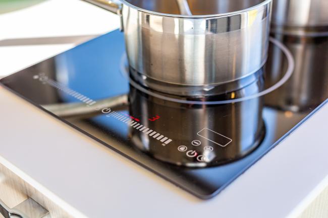 Stainless steel pot on a black glass induction cooktop with red digital controls in a campervan kitchen.