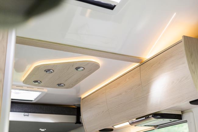 Campervan interior featuring light timber-look overhead cabinets and warm LED ceiling lighting.