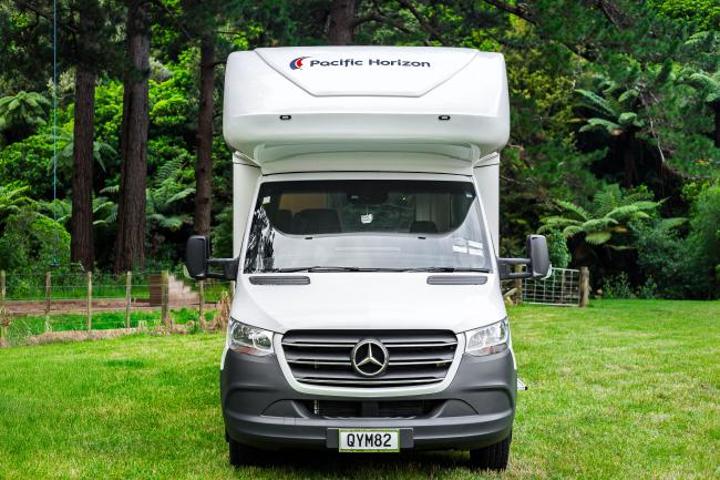 Front view of a white Pacific Horizon Mercedes campervan with license plate QYM82 parked on a green lawn.
