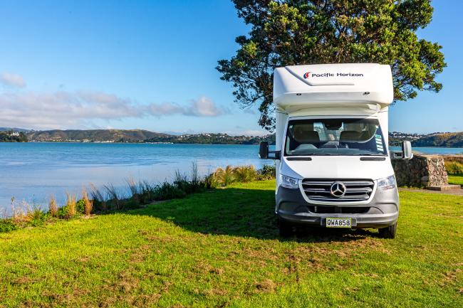 White Pacific Horizon campervan parked on grass beside water with hills in the background.