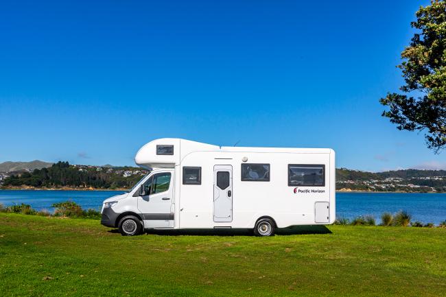 White Pacific Horizon campervan parked on a grassy field beside a blue lake under a clear sky.