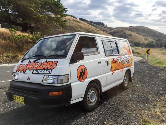 White Travellers Autobarn campervan parked on a gravel roadside with grassy hills in the background.