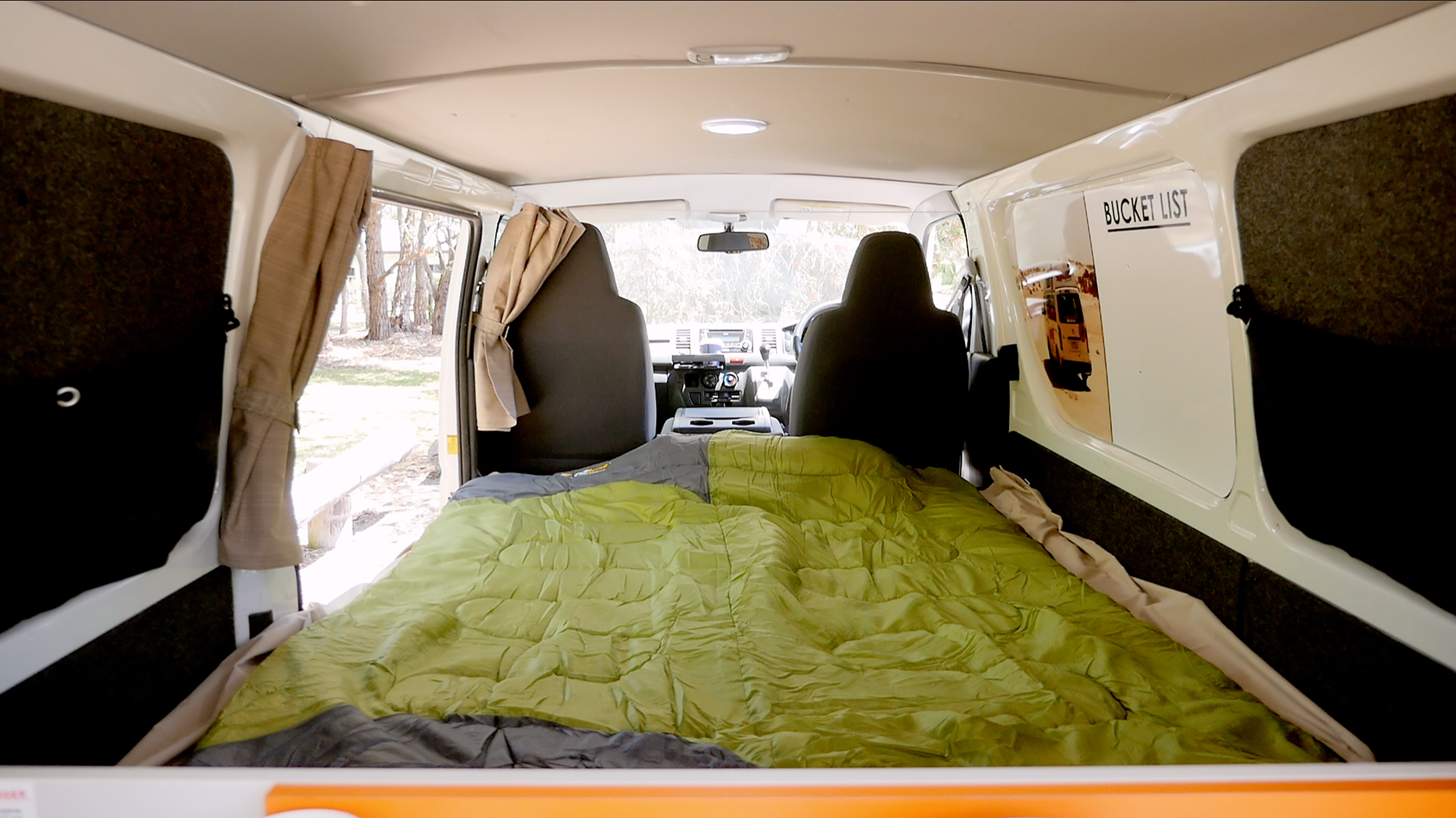 Interior of a campervan with a green sleeping bag on the bed, looking forward towards the front cabin.