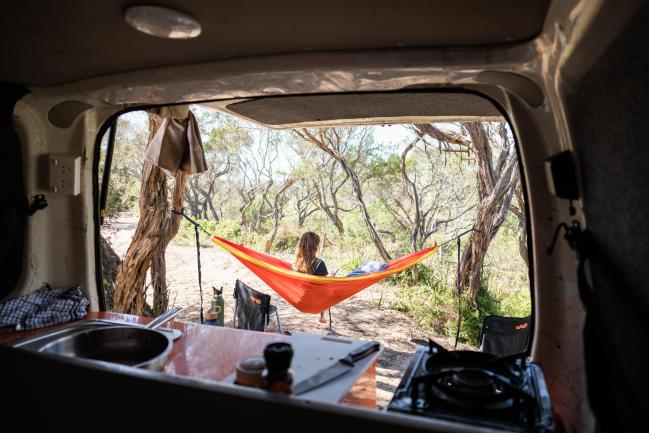Campervan interior view looking out to a person in an orange and yellow hammock strung between trees.