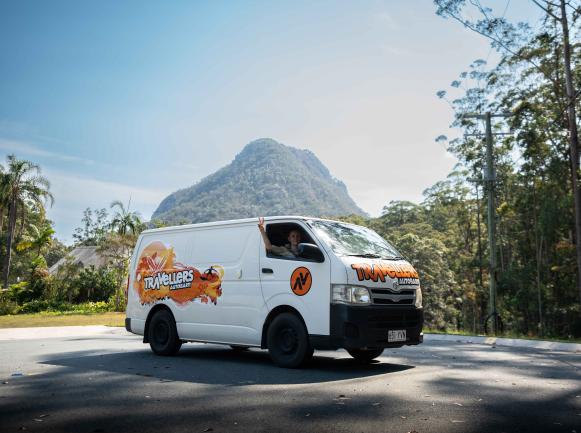 White Travellers Autobarn campervan with a waving driver, parked in front of a large mountain.