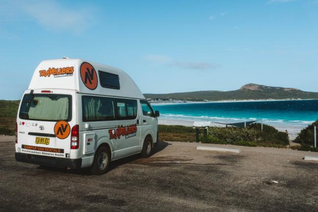 Travellers Autobarn campervan parked overlooking a turquoise beach and coastal headland.