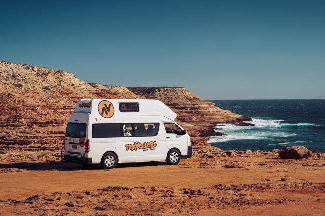 White Travellers Autobarn campervan parked on a red coastal cliff overlooking the ocean.
