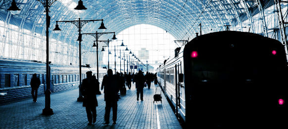 covered railway station with trains and silhouettes of hurrying people