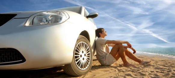 man sitting behind his white car rental staring at the sky in a brown sand