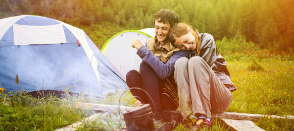 portrait of happy couple sitting near by the campfire with the tents