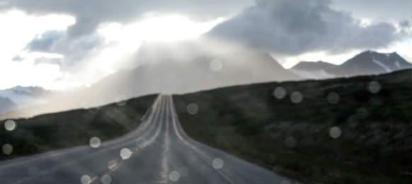 rain on a car windshield on a lonely mountain highway with storm clouds