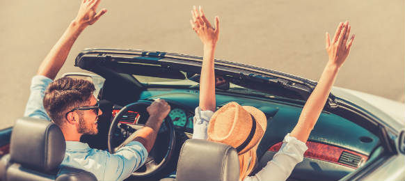 top view of cheerful young couple keeping arms raised while riding in their white convertible