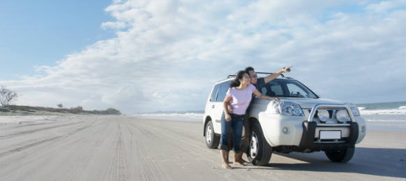 young couple is enjoying her honeymoon at the beach beside a car