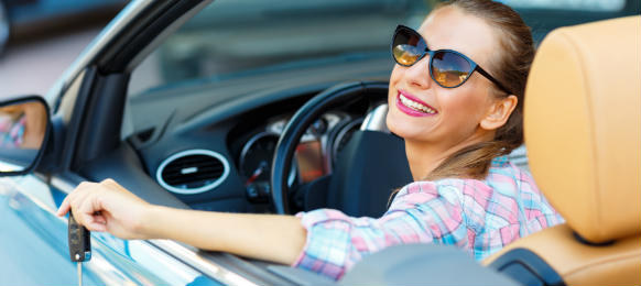 young pretty woman in sunglasses sitting in a convertible car rental with the keys in hand