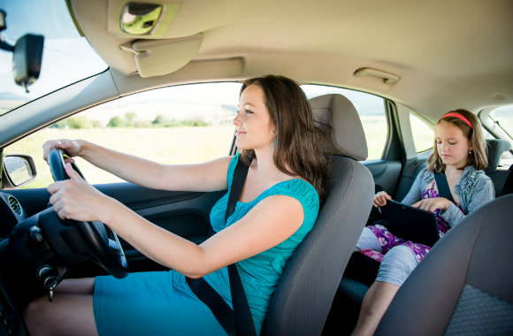 woman-driving-the-car-while-her-daughter-playing-an-ipad